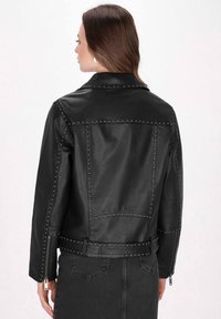 Giubbotto di pelle nera con accenti chiodati. Presenta una vita con cintura, polsini con zip e un design strutturato con dettagli di cucitura visibili.