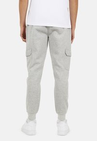 Szare dresowe spodnie z tapered leg, mankietami na kostkach i bocznymi kieszeniami cargo, zestawione z białymi sneakersami na jednolitym tle.