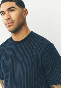 Mørkeblå t-shirt med lodrette细striber i kontrasterende blå nuancer, rund hals og korte ærmer. Stoffet virker glat og afslappet.