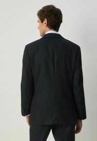 Giacca nera con un delicato motivo testurizzato, con uno spacco singolo e rever a punta. Chiusura a due bottoni e bottoni indossabili ai polsini.