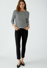 Schwarz-weiß gestreiftes Langarmtop mit Rundhalsausschnitt, kombiniert mit eng anliegenden schwarzen Jeans und spitzen schwarzen Ballerinas. Einfaches und klares Design.