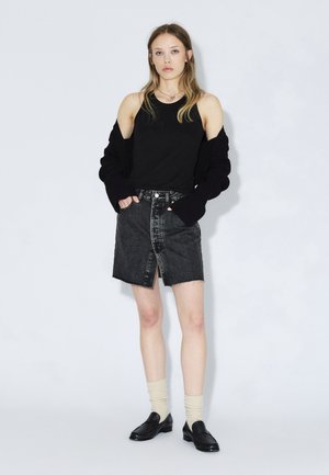 Sort tanktop under en sort oversized cardigan, kombineret med et gråt denimskørt med en frontslids. Færdiggjort med sorte loafers og cremefarvede sokker.