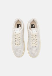 Vita sneakers med en slät ovandel i läder och mocka, perforeringar på tåkappan och en ljusgul gummisula. Snörningarna är beige.