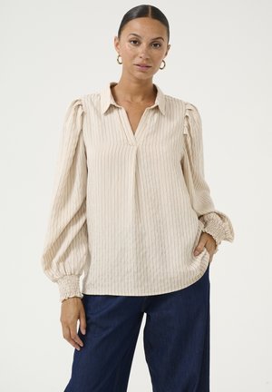 Beige striped blouse with a collar, v-neckline, and gathered puff sleeves. Soft, lightweight fabric with elasticated cuffs, paired with dark blue pants.