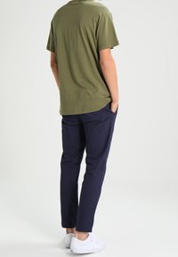 Camiseta de algodón verde oliva de corte relajado, combinada con pantalones tapered azul marino y zapatillas blancas, vista desde atrás.