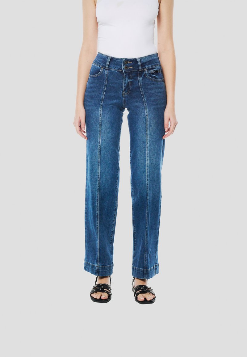 Blauwe denim wijde pijpen jeans met voorste naden, een hoge tailleband en contrasterende stiksels. Gecombineerd met zwarte sandalen met studs.