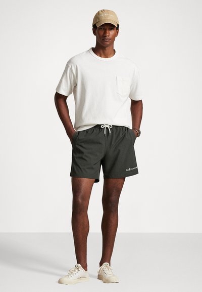 Svetlý krátky rukáv tričko s vreckom, skombinované s tmavozelenými šortkami s elastickým pásom a šnúrkou. Béžová čiapka.