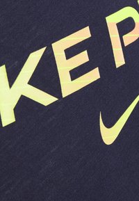 Camiseta de tejido azul marino que presenta un gran texto en amarillo y naranja que dice "NIKE", con un pequeño logotipo de swoosh de Nike, textura suave y diseño casual.