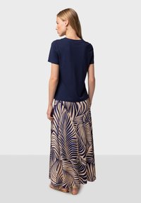 Marinblå t-shirt i kombination med en beige kjol med marinblå palmbladsmönster. T-shirten har en rund halsringning och korta ärmar.