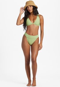 Bikini verde acanalado con top triangular y parte inferior de cintura alta, combinado con un sombrero de paja estilo cubo. Textura suave y diseño ajustado.