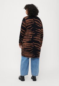 Suéter largo a rayas marrón y negro, hecho de material suave, combinado con jeans de pierna ancha azul claro y botas negras hasta el tobillo.
