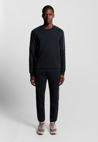 Zwarte sportieve sweatshirt met contrasterende schouderstrepen en bijpassende sweatpants. Het materiaal lijkt zacht, met geribde manchetten en een ontspannen pasvorm.