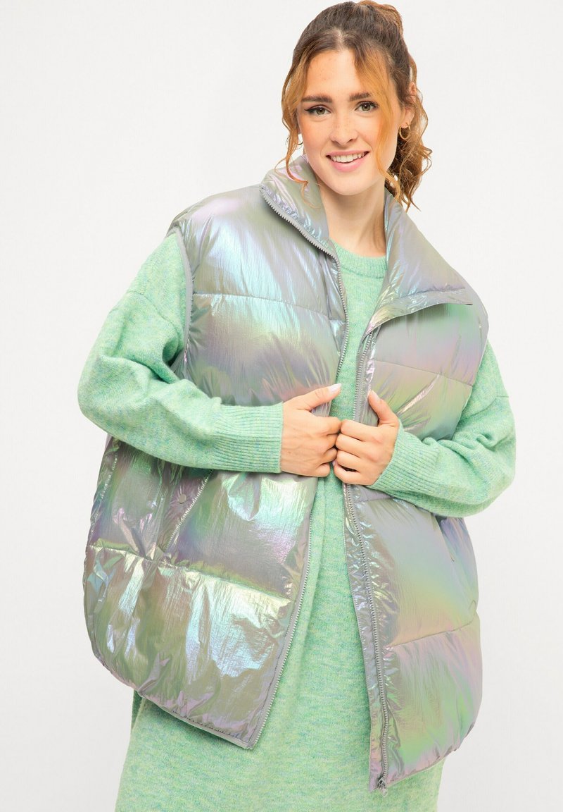 Iriscerende mouwloze puffer vest met een hoge kraag, rits aan de voorkant en geborduurd patroon, gecombineerd met een muntgroene gebreide trui.