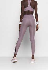 Soutien-gorge de sport violet et leggings assortis avec une taille haute et des accents noirs sur les côtés, associés à des chaussures de sport roses claires.
