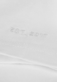 White cotton t-shirt with a textured finish and embroidered label reading "EST. 2017" in subtle white thread, positioned near the hem.