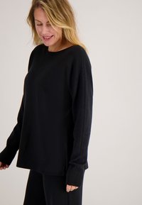 Zwarte gebreide trui met een losse pasvorm, ronde hals en geribbelde manchetten. Het materiaal lijkt zacht met een gladde textuur en een iets oversized vorm.