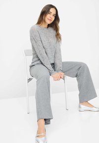 Grijze gebreide trui met een textuurafwerking, gecombineerd met grijze broek met visgraatpatroon en wijde pijpen. Zilveren flats maken de outfit compleet.