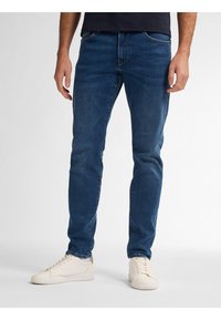 Jeans de mezclilla azul oscuro con un corte ajustado, que cuentan con bolsillos frontales y un diseño clásico de cinco bolsillos, combinados con zapatillas blancas.