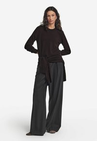 Czarny sweter z długim rękawem z wiązaniem w talii, w połączeniu z szerokimi szarymi spodniami o gładkiej teksturze materiału.