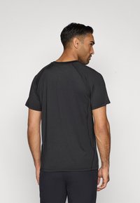 Černé tričko s krátkým rukávem s hladkým povrchem, raglánovými rukávy a kulatým výstřihem, z pohledu zezadu na jednobarevném pozadí.