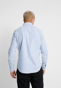 Chemise rayée bleu clair et blanche, fabriquée dans un tissu à texture lisse. Présente un col, des manches longues et un ourlet arrondi.