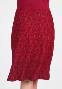 Roter Rock mit einem strukturierten Muster aus Tränenformen, aus gewebtem Stoff mit glatter Oberfläche. Der Saum ist leicht ausgestellt.