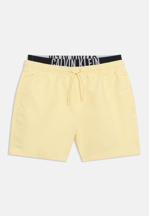 Heledu kollased paelaga ujumispüksid küljetaskutega ja nähtava musta-halli Calvin Kleini vöökohaga all.