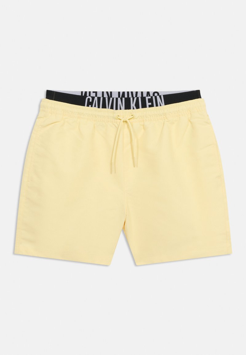 Απαλά κίτρινα μαγιό με κορδόνι, πλαϊνές τσέπες και ορατή μαύρη και γκρι ζώνη Calvin Klein από κάτω.