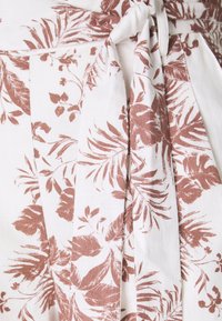 Witte stof met een bruine bloemmotief van bladeren, met een gestrikte riemdetail en plooien voor extra ontwerptextuur.