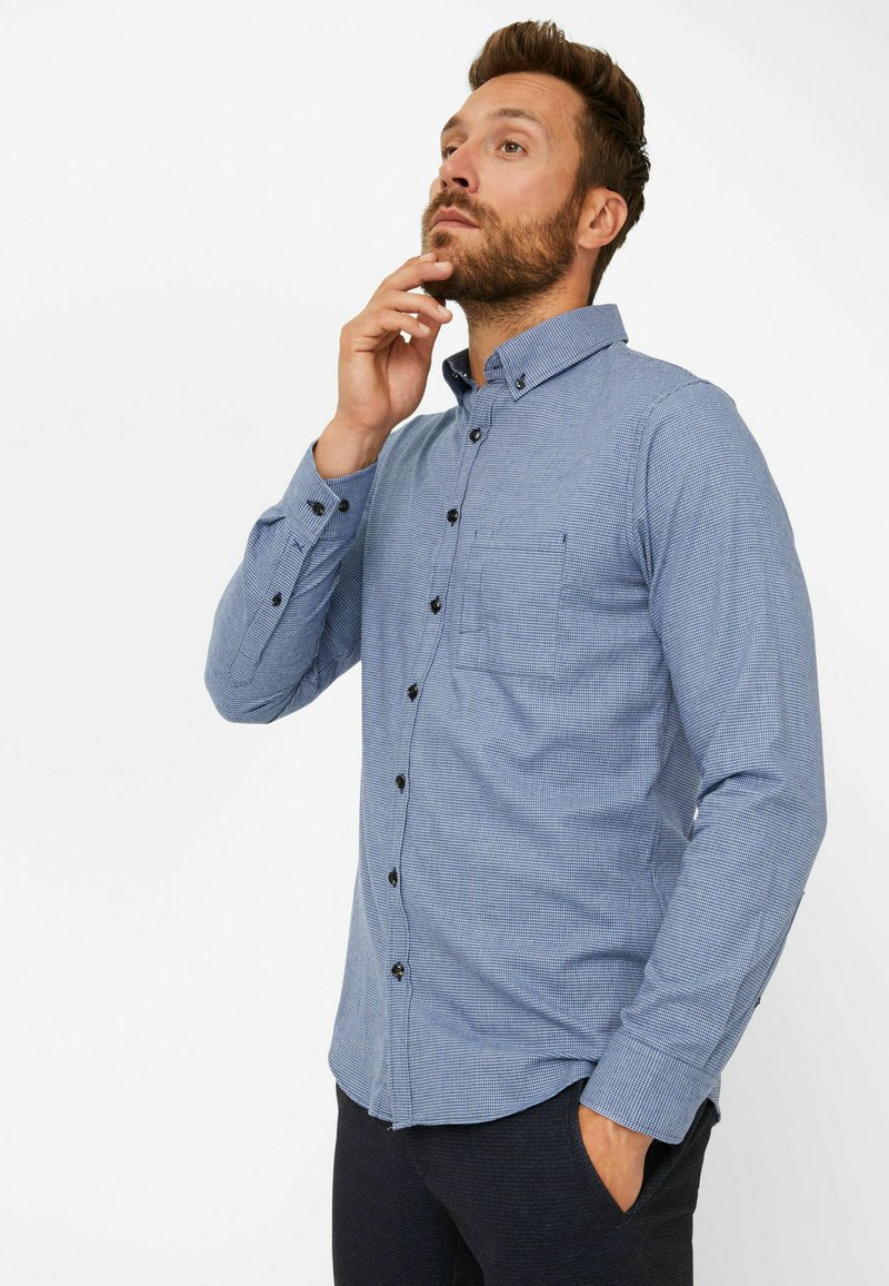 Blue checkered button-up shirt with black buttons, a chest pocket, and long sleeves. Made of lightweight fabric with a smooth texture.