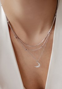 Collane a strati in argento con un pendant a forma di mezzaluna liscia, catene delicate con accenti sferici e superfici lucide e riflettenti.