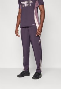 Lila Sportoutfit mit einem kurzärmeligen Oberteil mit weißem Text und passenden Hosen mit hellrosa Akzenten und drei Streifen an den Seiten.