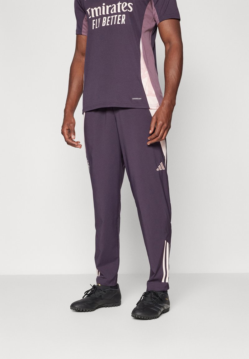 Lila Sportoutfit mit einem kurzärmeligen Oberteil mit weißem Text und passenden Hosen mit hellrosa Akzenten und drei Streifen an den Seiten.