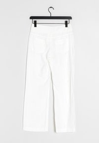 Valkoiset pellavahousut mustassa ripustimessa, suoraan lahkeeseen muotoon, kahdella takataskulla ja teksturoidulla kankaalla.