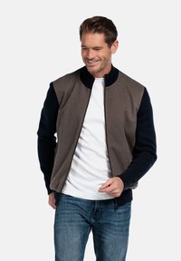 Zip-up jas met een bruine romp, donkerblauwe mouwen en een geribde kraag. Kenmerkt zich door een gladde stof met contrasterende texturen en een aansluitende pasvorm.
