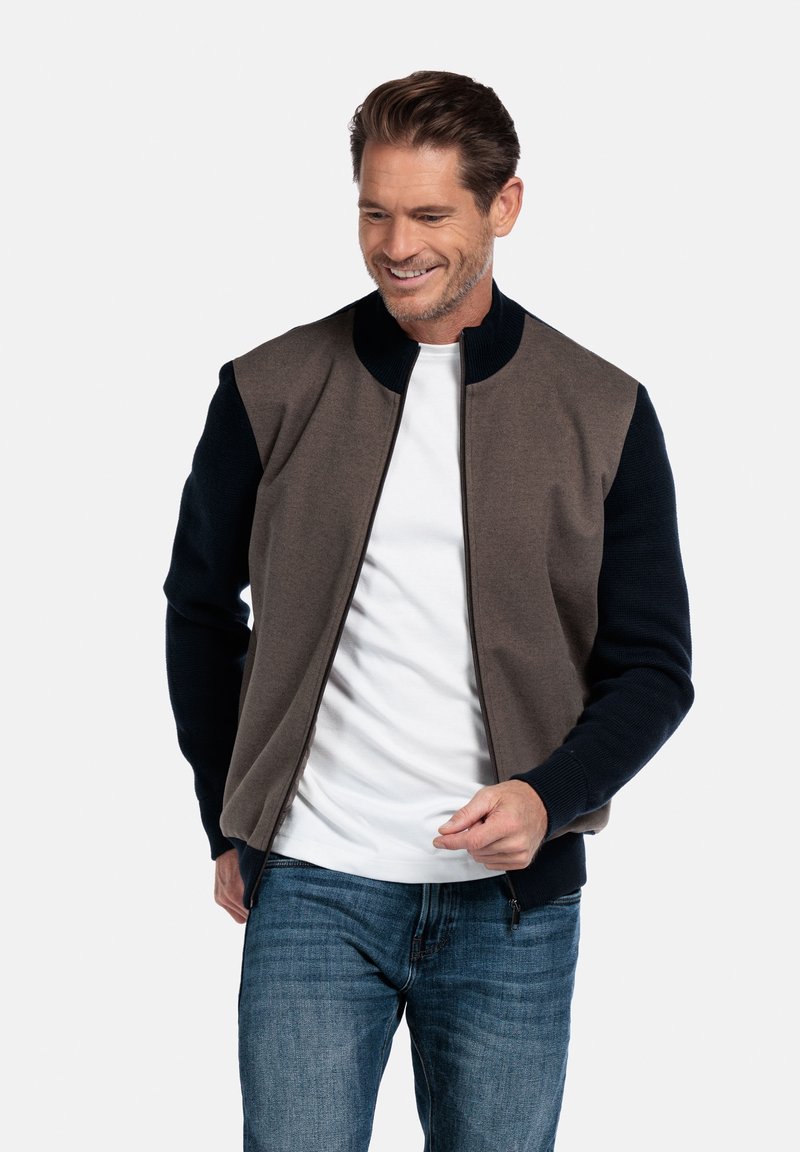 Zip-up jas met een bruine romp, donkerblauwe mouwen en een geribde kraag. Kenmerkt zich door een gladde stof met contrasterende texturen en een aansluitende pasvorm.