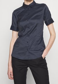 Mörkblå kortärmad skjorta med knappar, klassisk krage, slät yta och vikta ärmslut, figursydd design och svarta knappar.