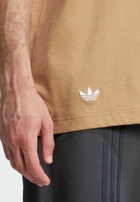 Tansk sommar t-shirt med en vit broderad logotyp vid fållen, tillsammans med strukturerade svarta träningsshorts med tre vertikala ränder.