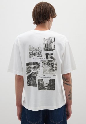 T-shirt bianco in cotone a maniche corte, con una grafica nera a collage sul retro, che include paesaggi urbani e elementi di testo.