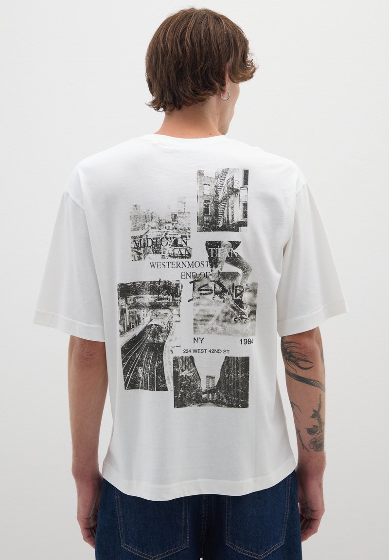 Camiseta de algodón blanca con mangas cortas, que presenta un collage gráfico negro en la parte trasera, incluyendo paisajes urbanos y elementos textuales.