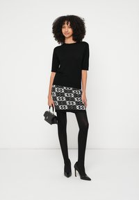 Top negru cu mâneci scurte, combinat cu o fustă mini cu model alb-negru, colanți negri și pantofi cu toc înalt. Geantă de mână mică, neagră.