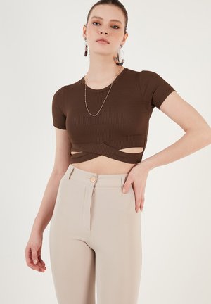 Braunes, geripptes Cropped-Top mit kurzen Ärmeln und Cut-out-Details. Kombiniert mit hoch taillierten beigen Hosen und einem Knopfverschluss.