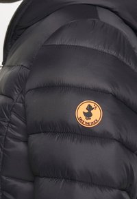 Doudoune noire avec une texture matelassée et un patch rond orange arborant un logo de canard, étiqueté "SAVE THE DUCK" sur l'épaule.