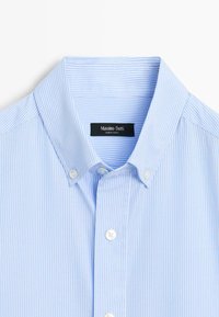 Camicia a righe azzurro chiaro con colletto button-down, bottoni bianchi e un'etichetta che recita "Massimo Dutti". Tessuto di cotone morbido.