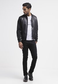 Zwarte leren bomberjack met ribgebreide manchetten, gedragen over een wit T-shirt, gecombineerd met zwarte jeans en zwarte veterschoenen. Minimalistisch ontwerp.