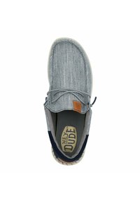Scarpa slip-on in tessuto blu con una suola grigia chiara, caratterizzata da una patch logo marrone chiaro e dettagli minimi delle stringhe.