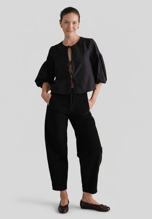 Czarna, krótka bluzka z bufkami i wiązaniem z przodu. Zestawiona z czarnymi, luźnymi spodniami i brązowymi balerinami. Gładka tekstura.