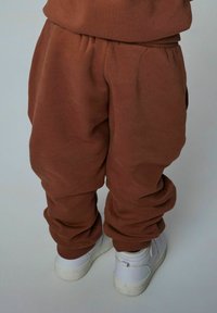 Brune bomulds-sweatpants med elastisk talje og manchetter, parret med hvide sneakers på en lys baggrund. Afslappet pasform og enkelt design.