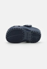 Navy blue molded rubber shoe sole with a textured tread pattern, circular logo detail, and raised edges for grip and support.