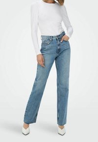 Lichtgewicht witte blouse met lange mouwen, gecombineerd met lichtblauwe high-waisted rechtoon jeans en witte pumps met een spitse neus.